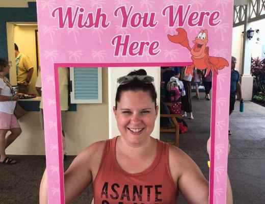 Woman smiling while holding up a sign that says "Wish you were here - Disney's Caribbean Beach Resort."
