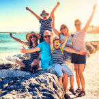A photo of a Multi-generation family vacation, with everyone holding their hands up and smiling by beach.