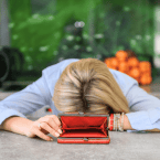 woman with her head on the desk and an open wallet with no money inside