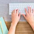 A woman typing on her keyboard with a pad of paper to the left of her