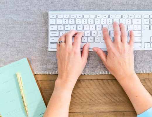 A woman typing on her keyboard with a pad of paper to the left of her