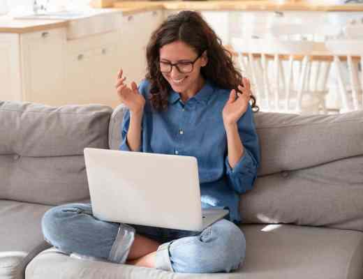 A woman sitting on the couch, in front of her computer, looking very excited.