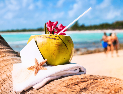 Tropical Coconut drink with a flower, sitting on a towel with a sea seat perched against the coconut.